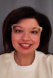 A smiling woman wearing clear, cat-eye glasses and a white top.